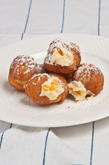 Top view, close up of four freshly baked, homemade, warm orange and chocolate ricotta filled donuts, sprinkled with powdered sugar on a round, white plate on a white towel with blue stripes 