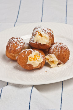 Top view, close up of four freshly baked, homemade, warm orange and chocolate ricotta filled donuts, sprinkled with powdered sugar on a round, white plate on a white towel with blue stripes 