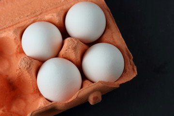 Four raw uncooked white eggs in an orange box with free cells close on a dark background