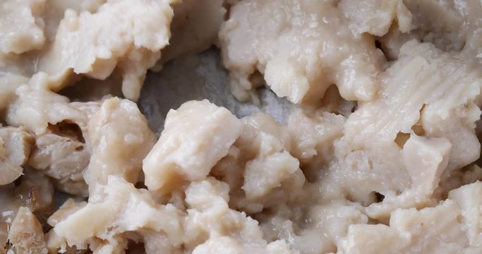 Close video stirring clumpy fish chowder in a pan with a black spoon for cooking.