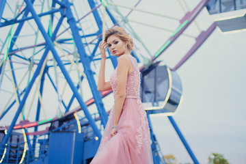 Young beautiful woman in long pink evening dress walking path in park. Fashion style portrait of gorgeous beautiful girl outdoors