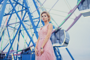 Young beautiful woman in long pink evening dress walking path in park. Fashion style portrait of gorgeous beautiful girl outdoors