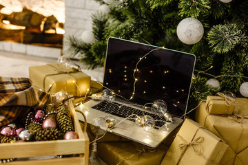 Image of open laptop with white screen on wooden table in front of christmas tree background. For mockup
