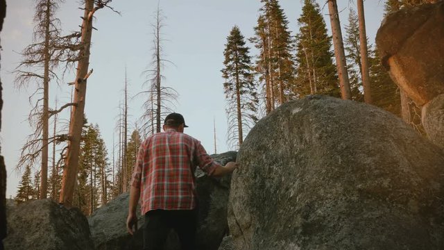 Camera follows young local man hiking, climbing up on big forest stones to watch epic sunset at Yosemite slow motion.