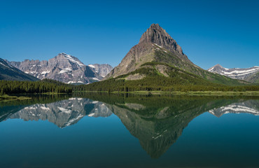 Naklejka premium Odbicie jałowej góry górującej nad jeziorem Swiftcurrent w piękny letni dzień w Glacier National Park