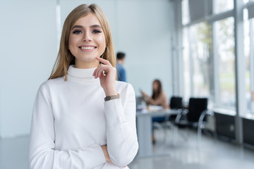 Fototapeta premium Beautiful young business lady is looking at camera and smiling while her colleagues are working in the background.