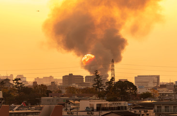 Orange sphere of setting sun descends into smoke billowing from large neighborhood fire