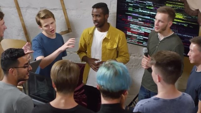 High angle view of group of multiethnic young people standing in circle and discussing topic at coding workshop