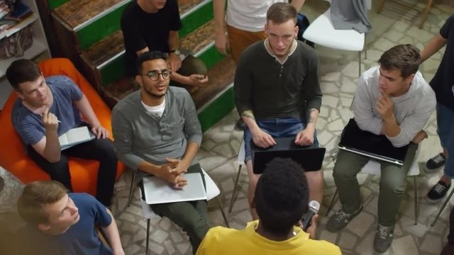 High angle view of young black man delivering presentation at workshop, group of listeners discussing topic with him