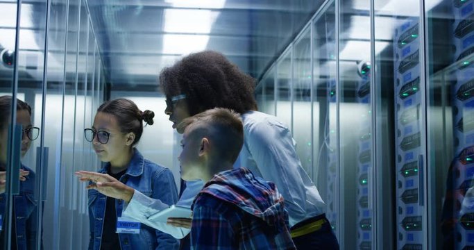 Medium shot of a young female technician with digital pad showing around children in a server park data center