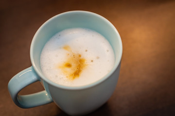Cappuccino in a pastel blue cup on a brown table, visible white coffee foam