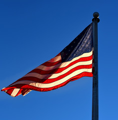 Naklejka premium A closeup of the American flag backlit with a beautiful clear blue sky.