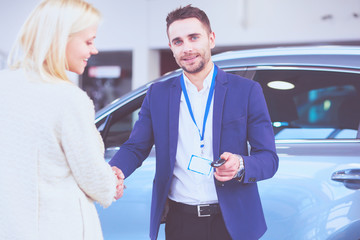 Image of car dealer handshaking with happy female in automobile center