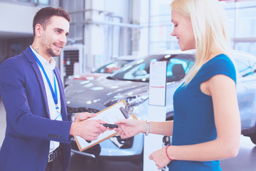 Car salesman sells a car to happy customer in car dealership and hands over the keys