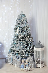 New Year's Decor in a photo studio in gray and white. A snow-white Christmas tree, gifts and lanterns, against the background of a white wall with a garland