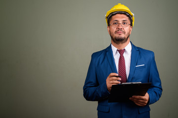 Bearded Persian businessman wearing hardhat against colored back