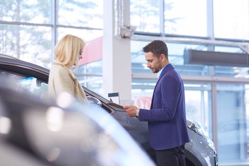 Dealer with woman stands near a new car in the showroom