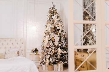 Interior of cozy room decorated in Christmas Happy new Year style. No people. An empty sofa, Christmas tree with presents under it. Selective focus. Happy NY mood. A lot of white sun light