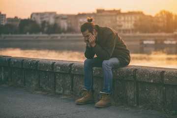 Depressed modern businessman sitting by the river.