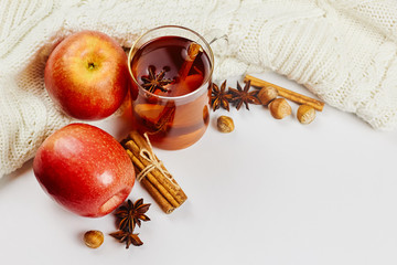 Glass cup of hot spicy tee with apple slices, cinnamon and anise on white knitted background with...