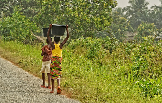 African teenagers carry a luggage on their heads. Young African girls walk along the road. Countryside. Lifestyle in developing countries of Africa. Ghana, Accra - January 31, 2017
