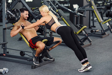 Fototapeta na wymiar Muscular healthy guy and his sporty girlfriend training together in the gym. Lovely couple training together at the gym. Fitness and bodybuilding concept.