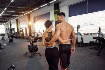 Obraz na płótnie Canvas Muscular healthy guy and his sporty girlfriend training together. Portrait of young sports couple standing in the gym. Back view.