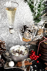 Christmas, luxury xmas, silver cup of sweet cream, and glass of champagne on black table, with sweets, cinnamon, aniseed, winter cone, and glass