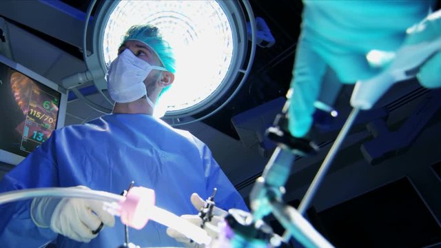 Medical Caucasian surgical team in scrubs performing Laparoscopy surgery on the patient in sterile operating theatre using video camera technology 