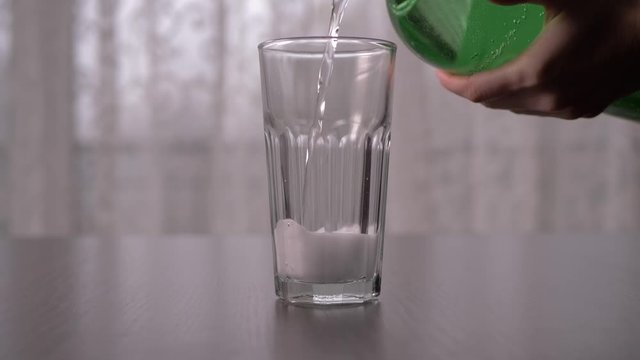 Pouring transparent sparkling soda into tall glass in slow motion, straight ahead shot