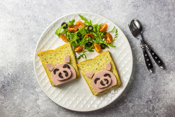 Funny animal sandwich for kids shaped cute pig with boiled sausage and olives on white plate on grey background, food art idea. Top view