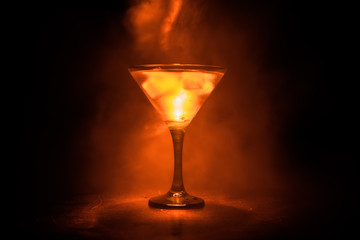 Martini in fire concept. Glass of famous cocktail Martini burning in fire at dark toned foggy background.