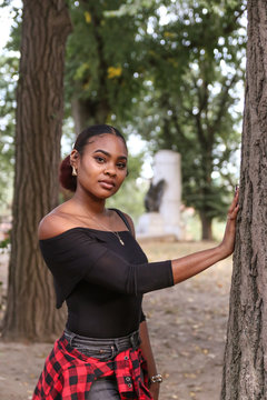 Black woman posing by trees at the park
