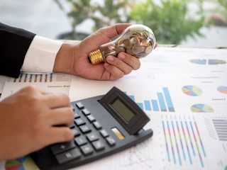 Hands of businessman holding a light bulb and use calculator calculate the costs need to be...