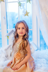 Cute little girl with curly hair at the window in anticipation of Christmas and New Year's magic