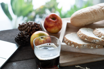 Breakfast served with glass of coffee, bread, apple and laptop on the wood table. Healty breakfast before working.