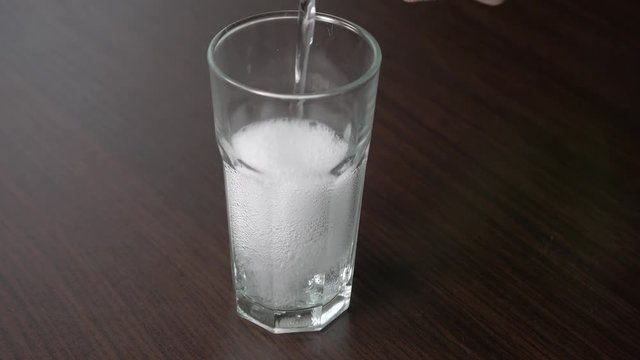 Pouring transparent soda into a tall glass on a wooden table