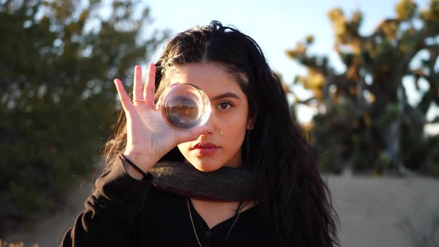 Zoom in to a cute girl witch or wizard in a fantasy world staring into her magic crystal ball in slow motion while casting a mysterious spell.