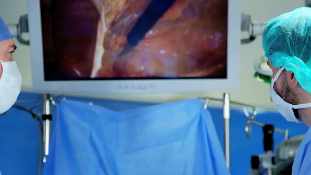 Medical Laparoscopic surgical training operation transmitted on hospital monitor performed by Caucasian male wearing surgical gloves and scrubs 