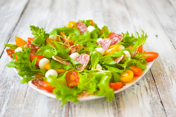 Arugula salad \ Salad with rocket salad, cherry, olives, cheese, mozzarella, blue cheese, sausage on a light wooden background