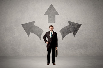 Charming businessman in doubt, choosing from three directions in front of a grey wall
