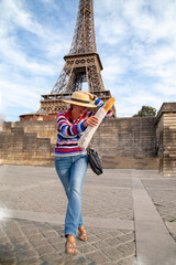 happy woman in a striped sweater and straw hat with a baguette in her hands jumping against the background of the Eiffel Tower