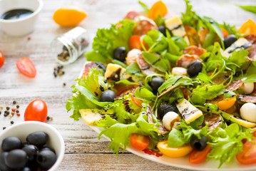Arugula salad \ Salad with rocket salad, cherry, olives, cheese, mozzarella, blue cheese, sausage on a light wooden background