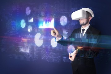 Elegant businessman in DJI goggles handling 3D reports and charts around him
