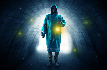 Ugly man in raincoat walking with glowing lantern in a dark tunnel