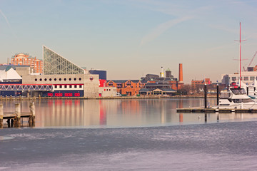 Baltimore Inner Harbor panorama before a winter sunset. City buildings along harbor piers with reflection in ice, Maryland, USA.