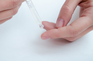 hands of woman Dropping serum  moisturizer of face into clear white bottle soft light background. Beauty and spa Concept.