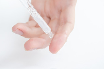 hands of woman Dropping serum  moisturizer of face into clear white bottle soft light background. Beauty and spa Concept.