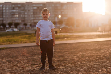 Fototapeta na wymiar a disgruntled boy in a white t-shirt in full growth looks at the camera in the sunset light
