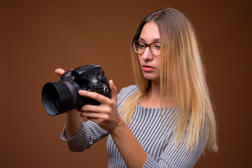 Young beautiful woman photographer holding DSLR camera against brown background